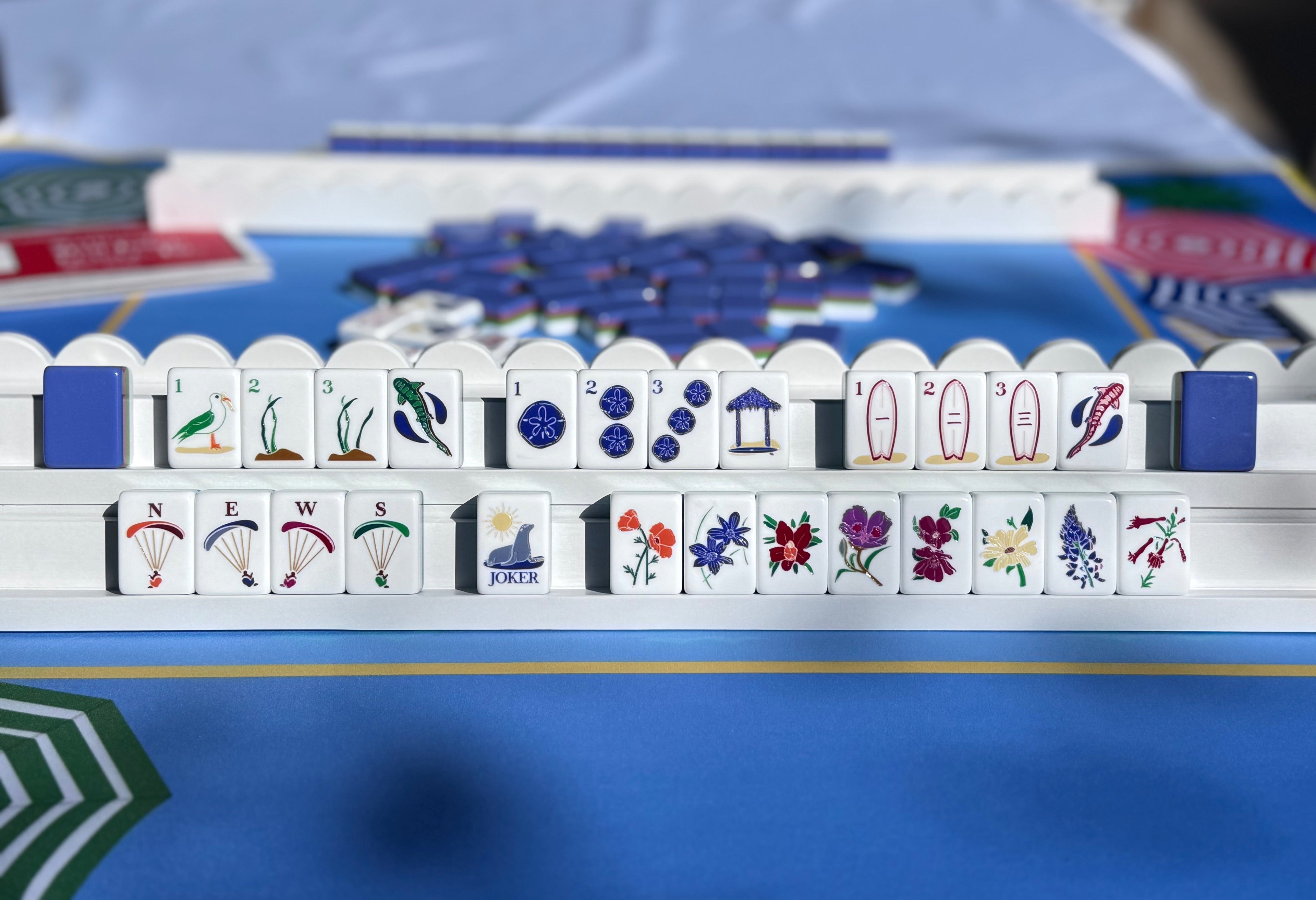 Close-up of a Mahjong game setup on a blue tablecloth with tiles and board visible.